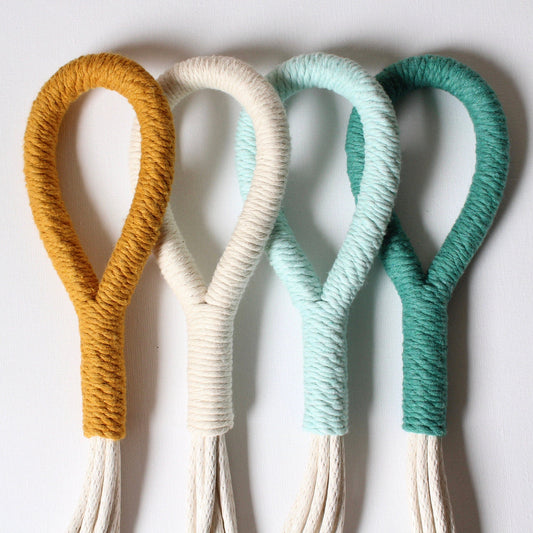 Four rope wall hooks in mustard yellow, cream, mint green, and teal, arranged vertically against a plain white background.