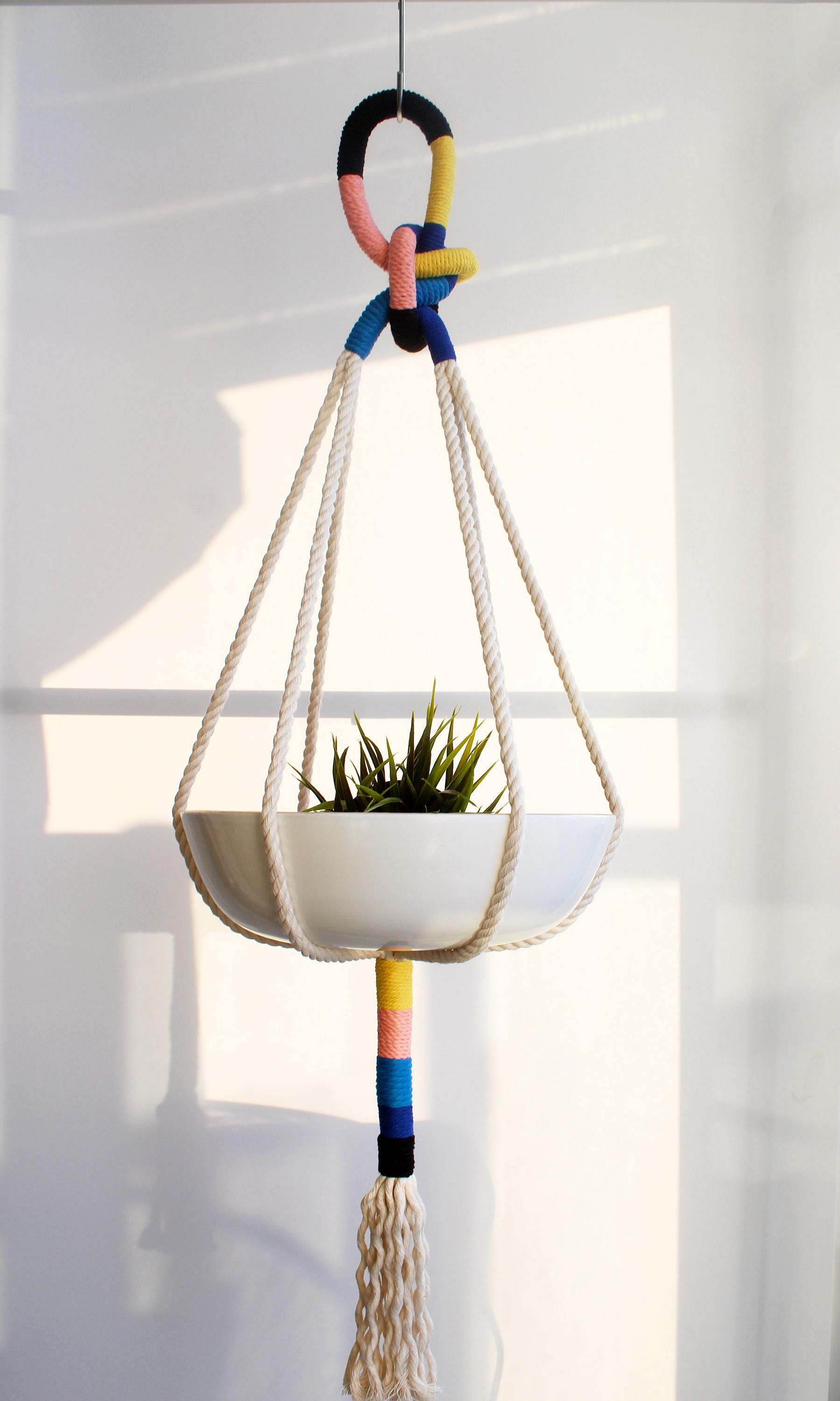 Handmade 37-inch macrame plant hanger with tassels, featuring color-block thread wraps in bright yellow, dusty pink, black, and deep midnight blue holding a houseplant.