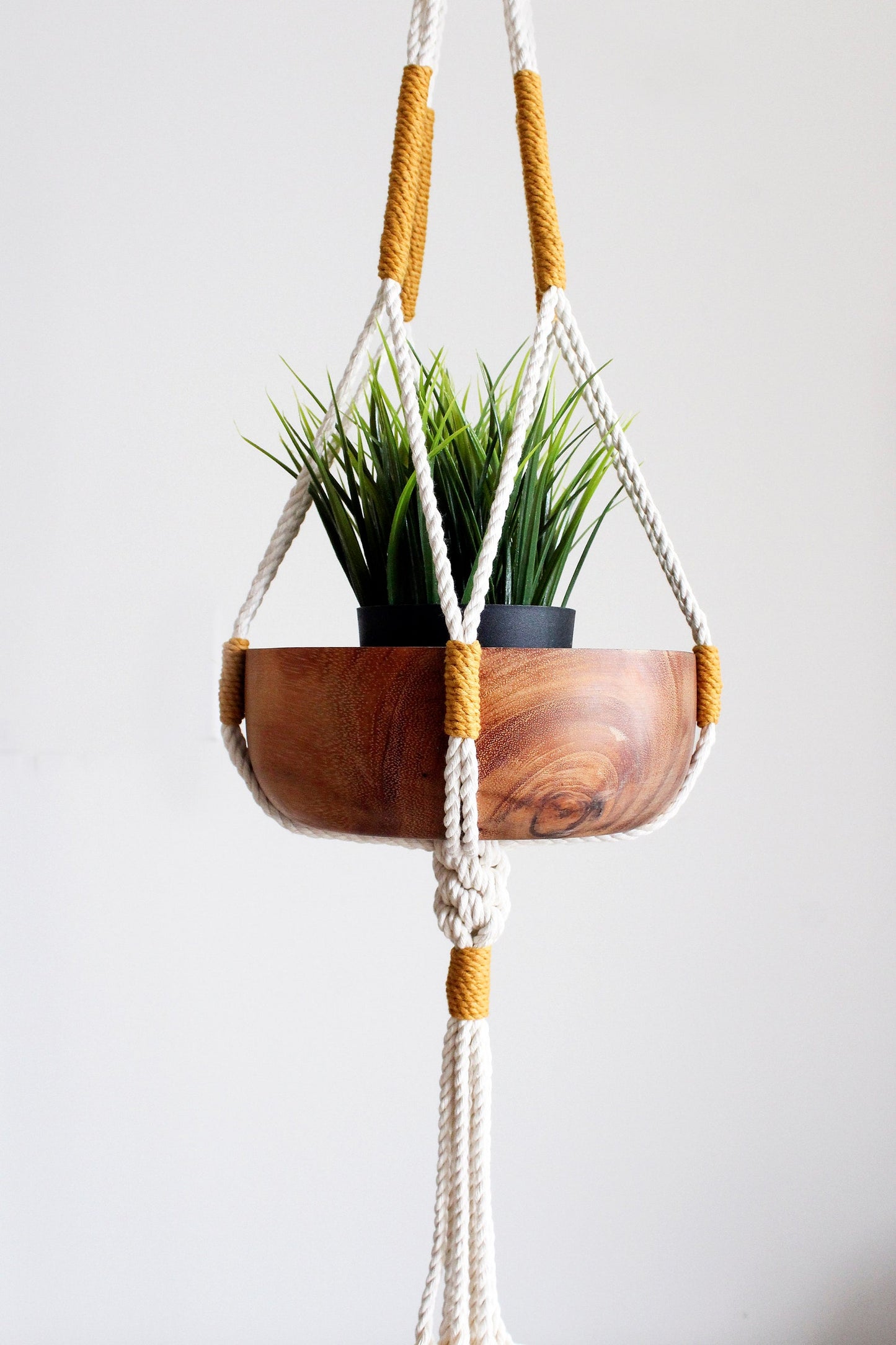 Handmade off-white cotton macrame plant hanger holding a green potted plant against a neutral wall by Freefille
