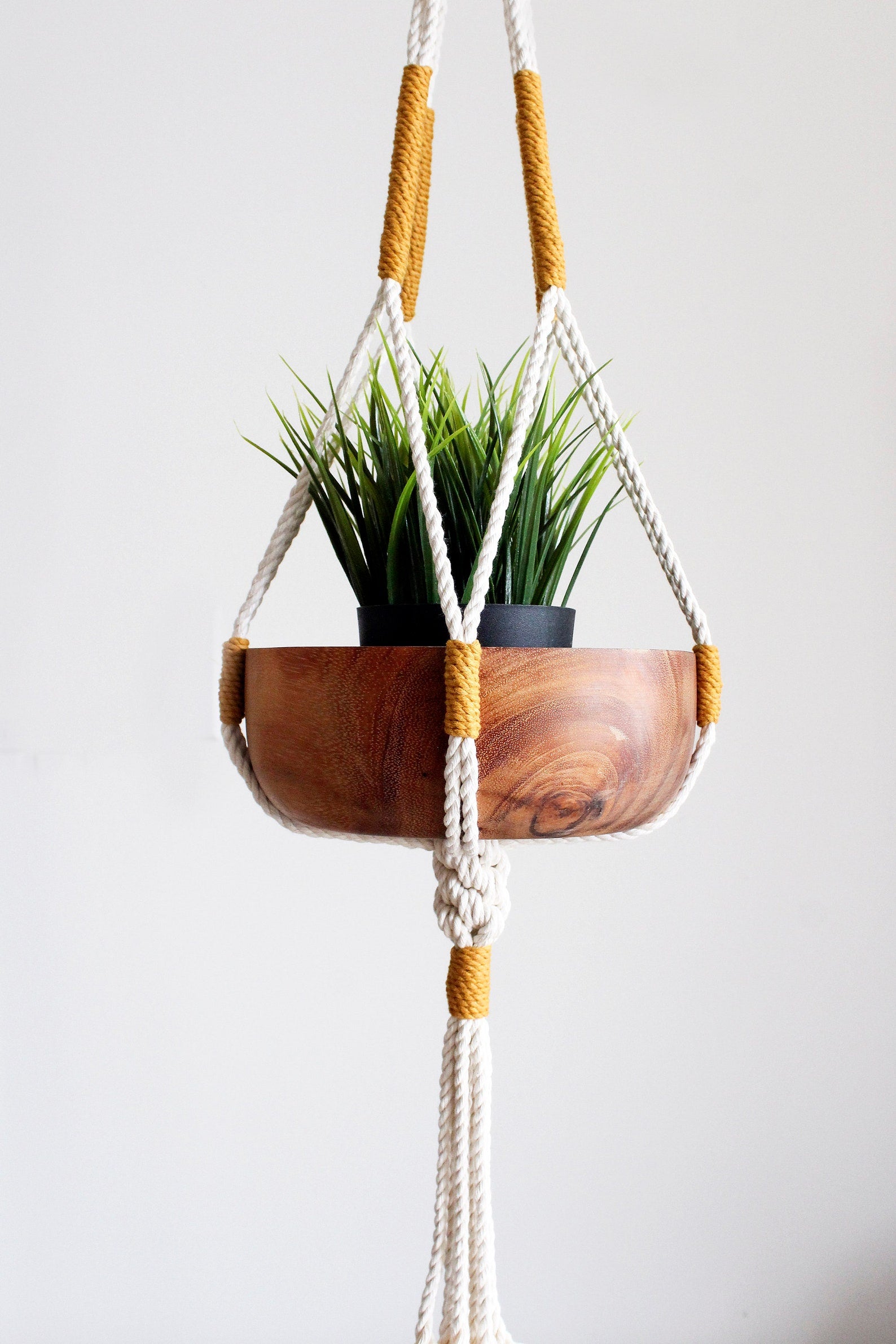 Handmade off-white cotton macrame plant hanger holding a green potted plant against a neutral wall by Freefille