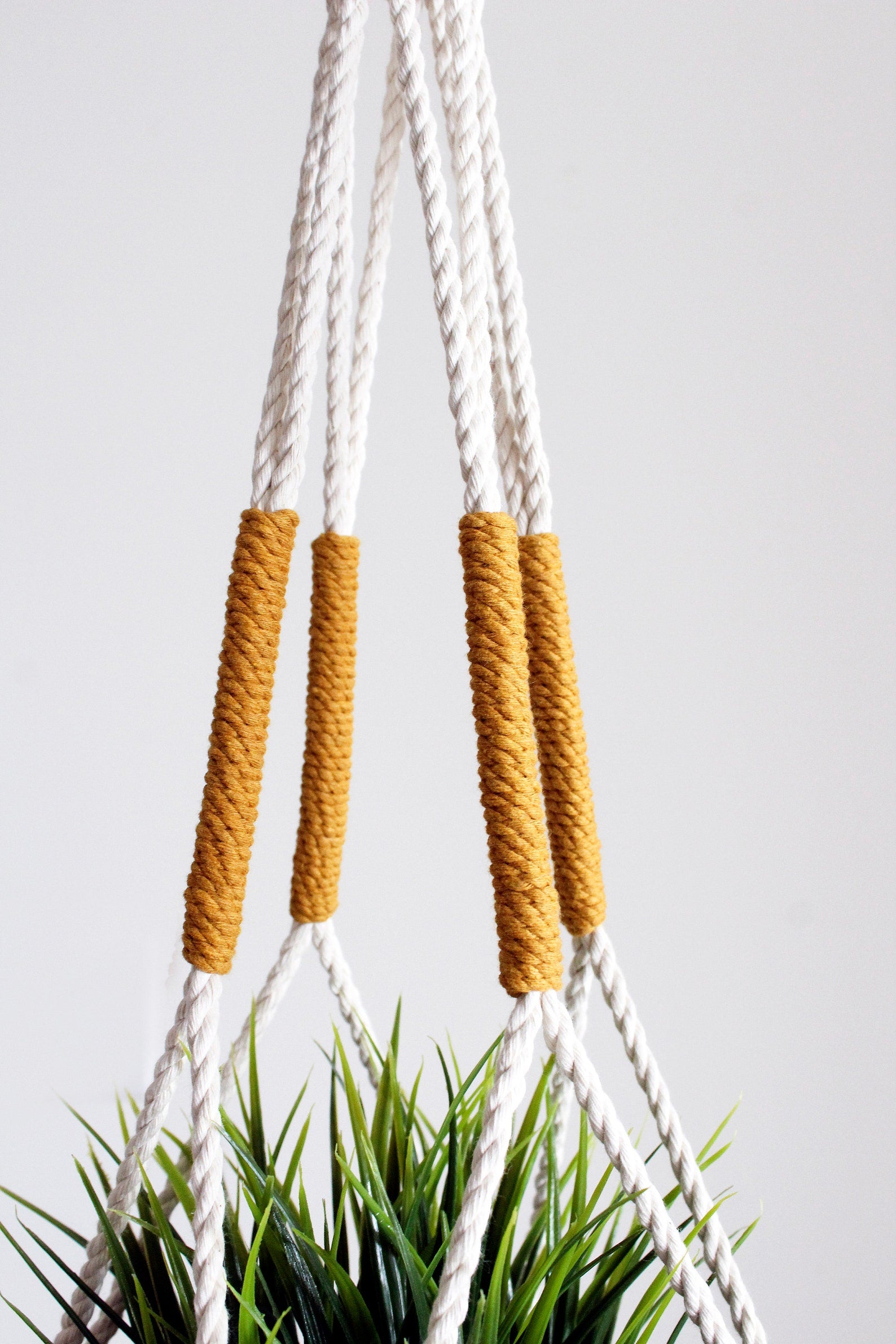 Handmade cotton macrame plant hanger in mustard yellow against a neutral wall by Freefille