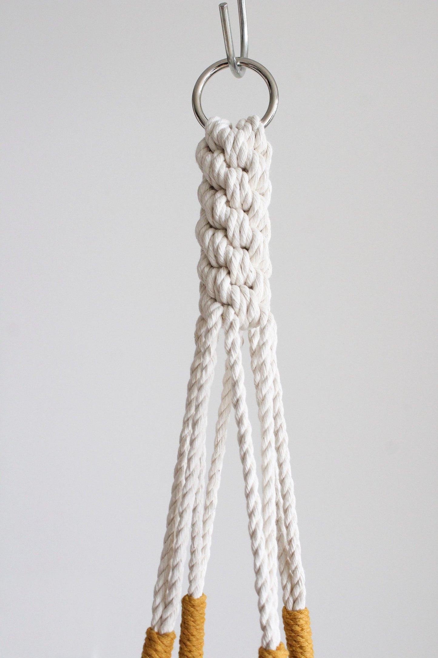 Handmade cotton macrame plant hanger in mustard yellow against a neutral wall by Freefille