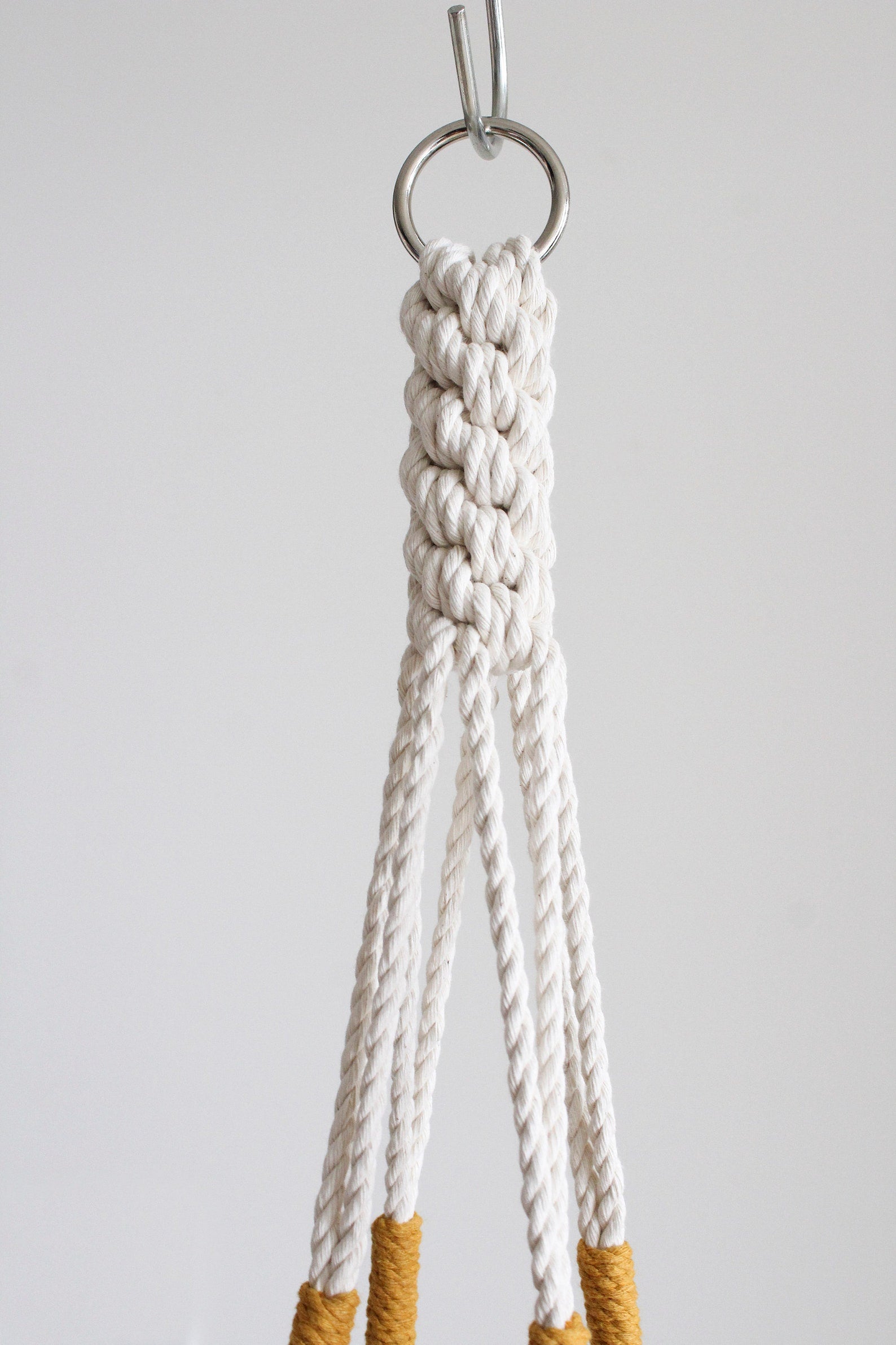Handmade cotton macrame plant hanger in mustard yellow against a neutral wall by Freefille