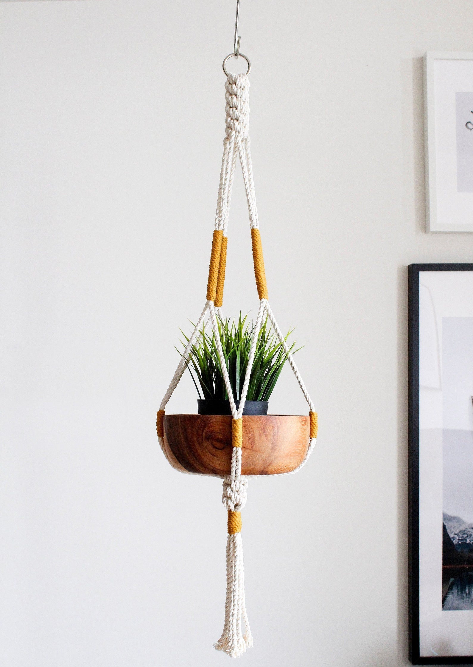 Handmade cotton macrame plant hanger in mustard yellow holding a wood potted plant against a neutral wall by Freefille