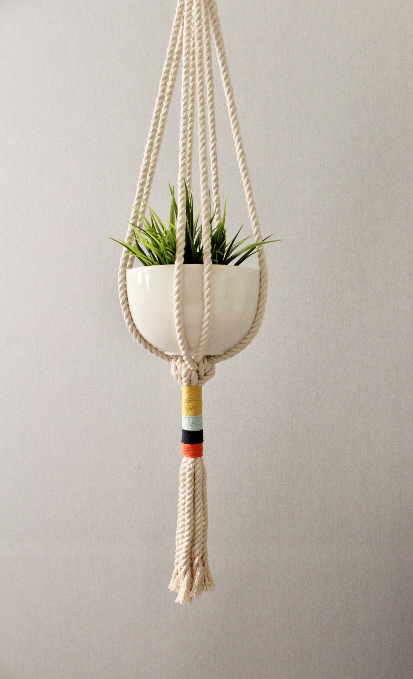 Modern cream macramé plant hanger with colorful navy, orange, mint blue, and yellow wrapped cord details by Freefille