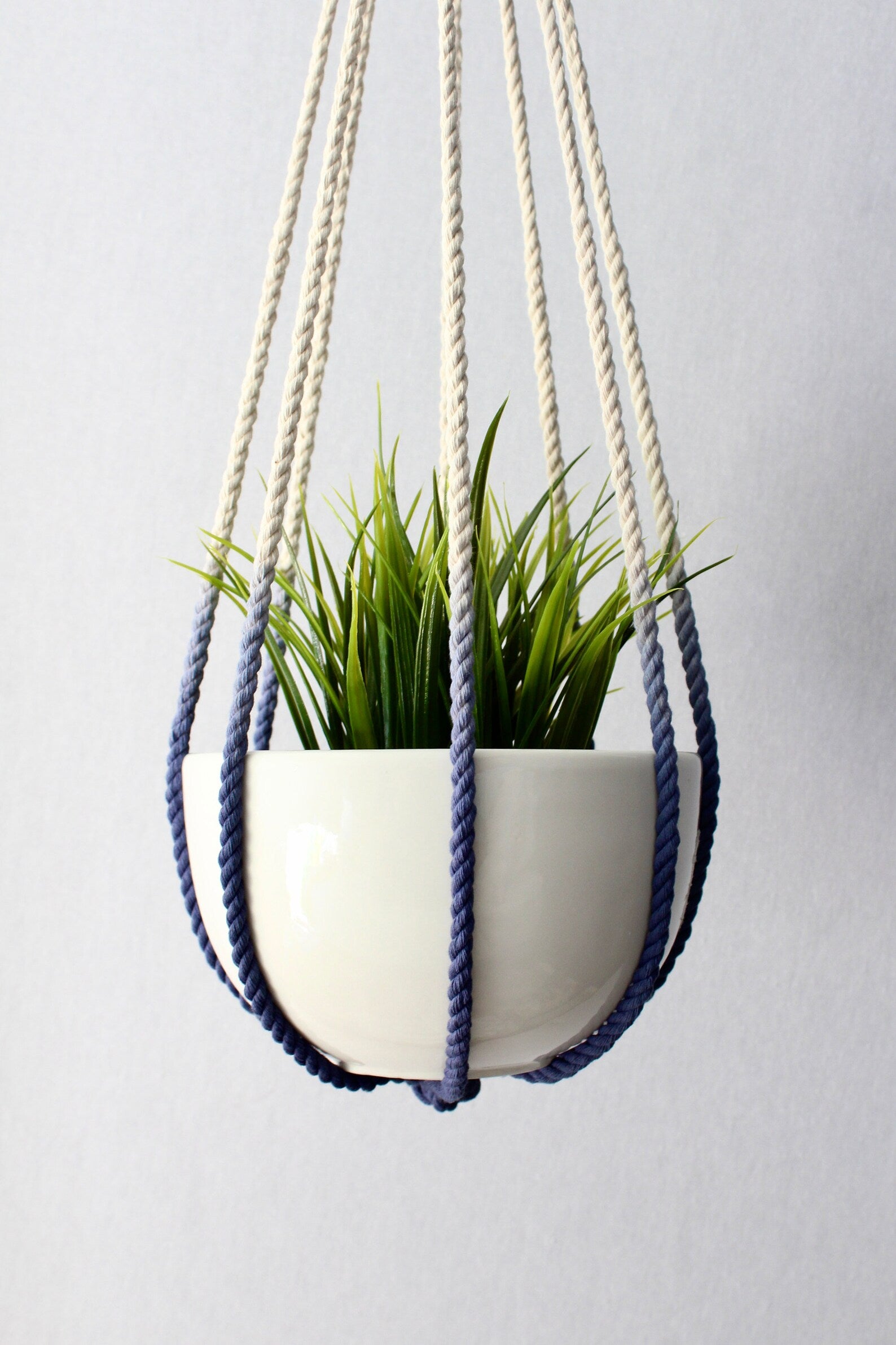 Handcrafted tassel-free macrame plant hanger in navy blue and cream color-block design holding a white potted plant.