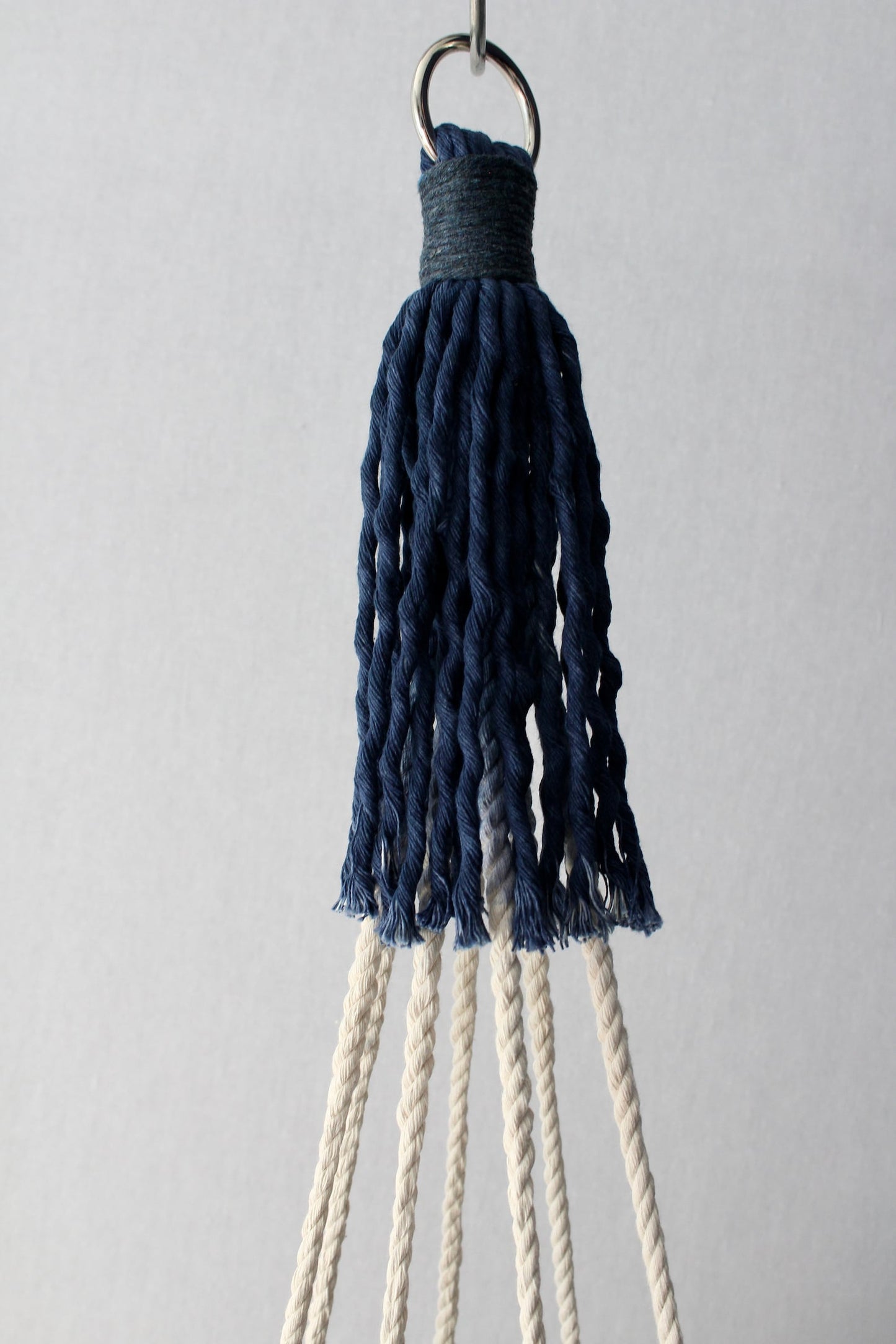 Handcrafted tassel-free macrame plant hanger in navy blue and cream color-block design holding a white potted plant.