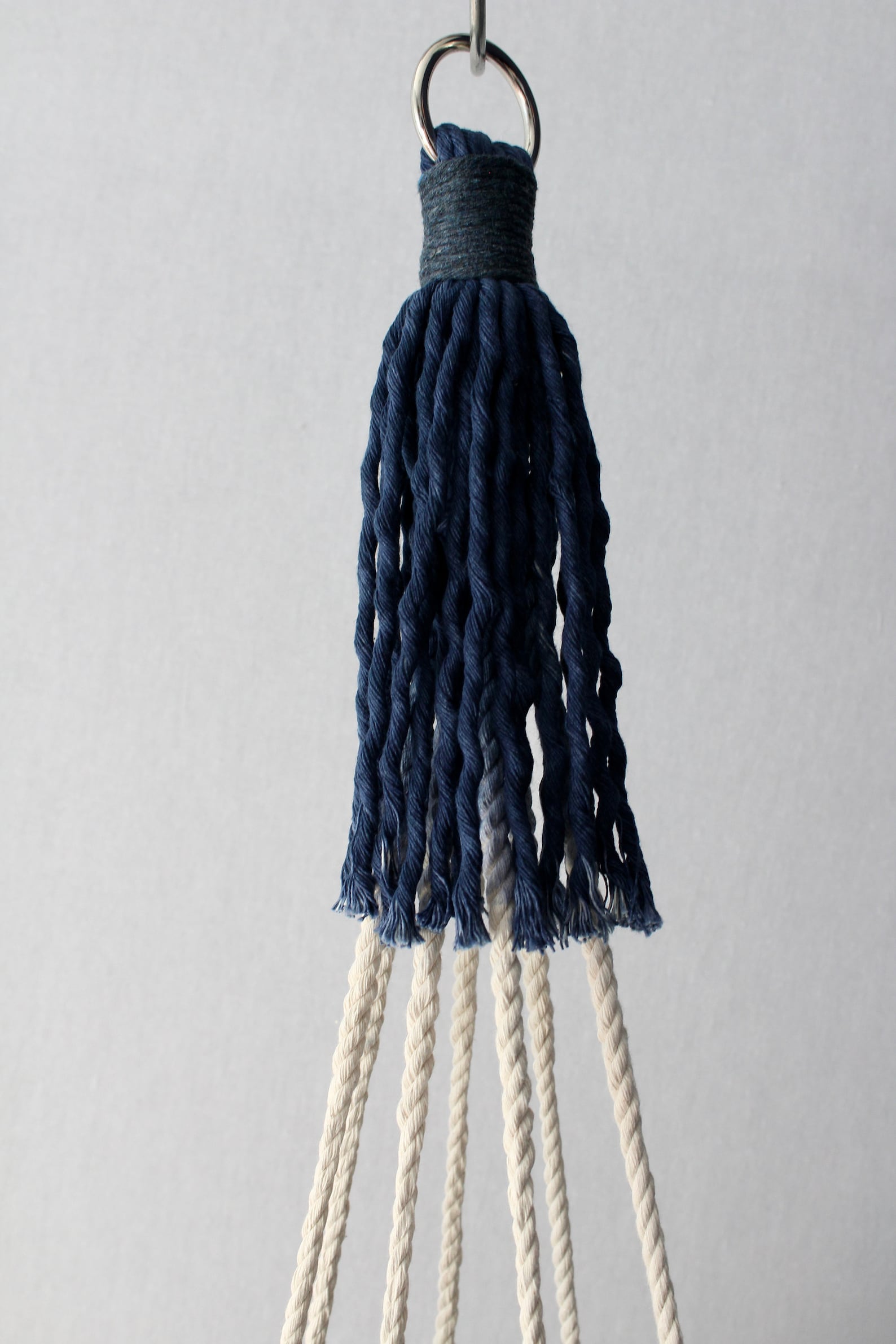 Handcrafted tassel-free macrame plant hanger in navy blue and cream color-block design holding a white potted plant.