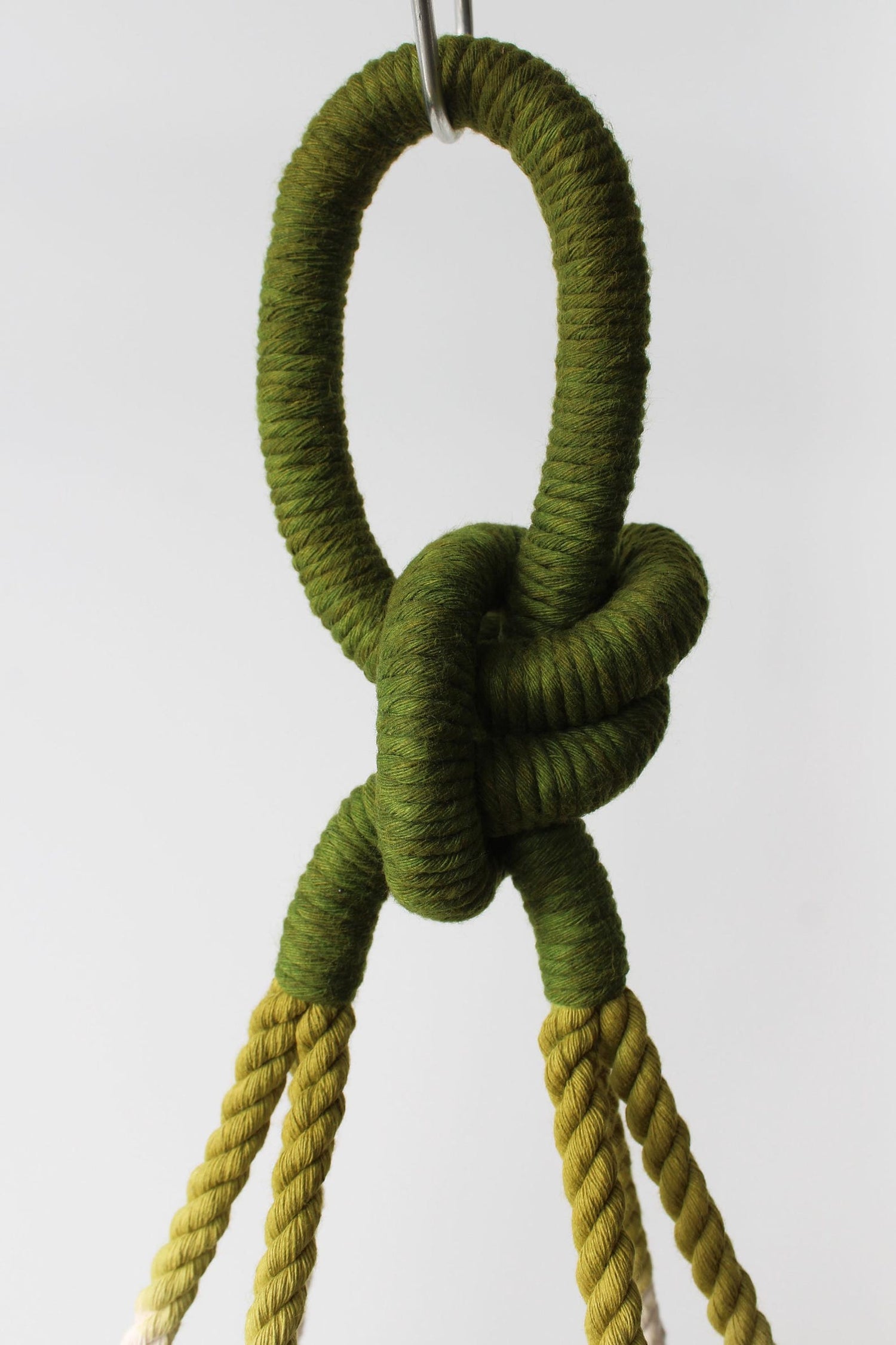 Olive and moss green ombre macramé plant hanger holding a white ceramic bowl pot with greenery by Freefille