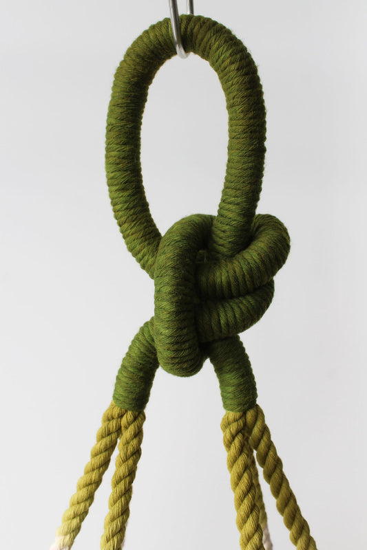 Olive and moss green ombre macramé plant hanger holding a white ceramic bowl pot with greenery by Freefille