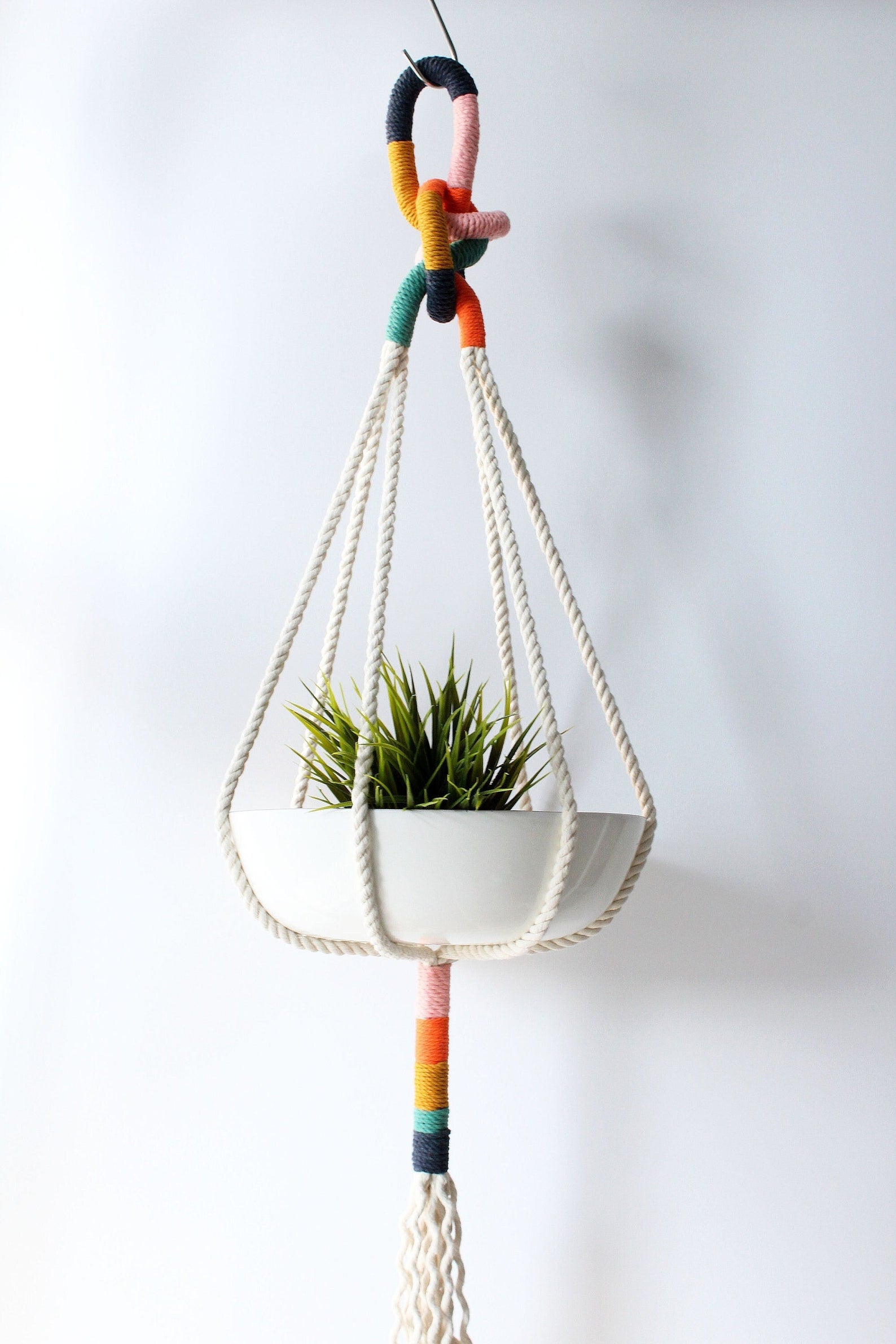 Colorful macrame plant hanger with a white planter holding a succulent on a plain background made by Freefille