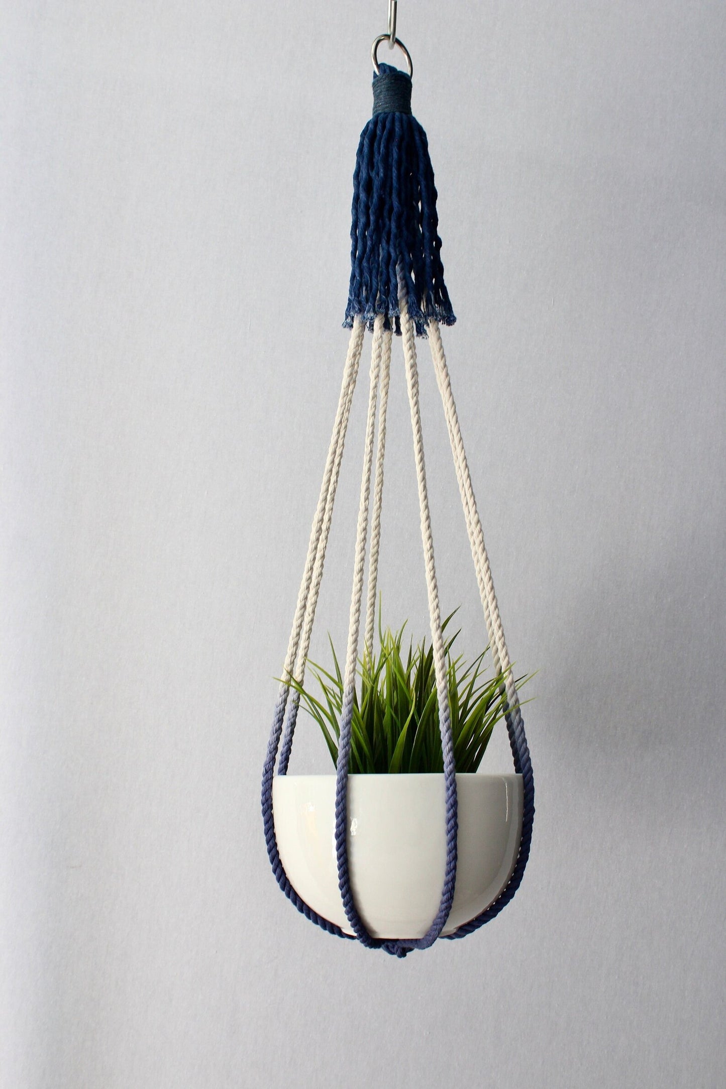 Handcrafted tassel-free macrame plant hanger in navy blue and cream color-block design holding a white potted plant.