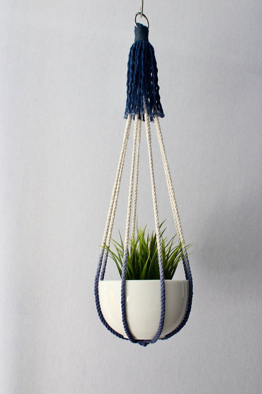 Handcrafted tassel-free macrame plant hanger in navy blue and cream color-block design holding a white potted plant.